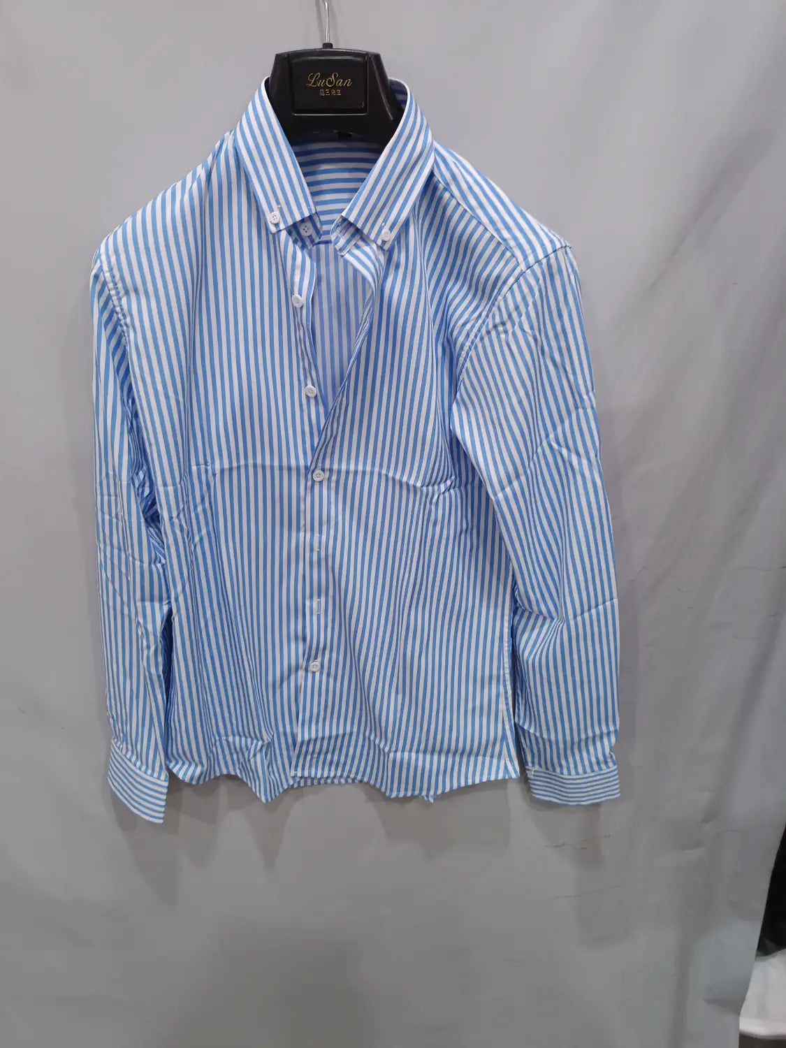 Chemise décontractée à manches longues rayée verticalement bleu clair et blanc pour hommes, avec col classique présenté sur un cintre noir.