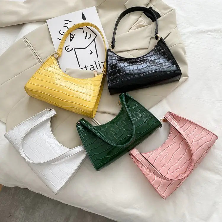 A collection of five vibrant crocodile embossed pu leather crescent messenger bags in yellow black white green and pink with a glossy finish.