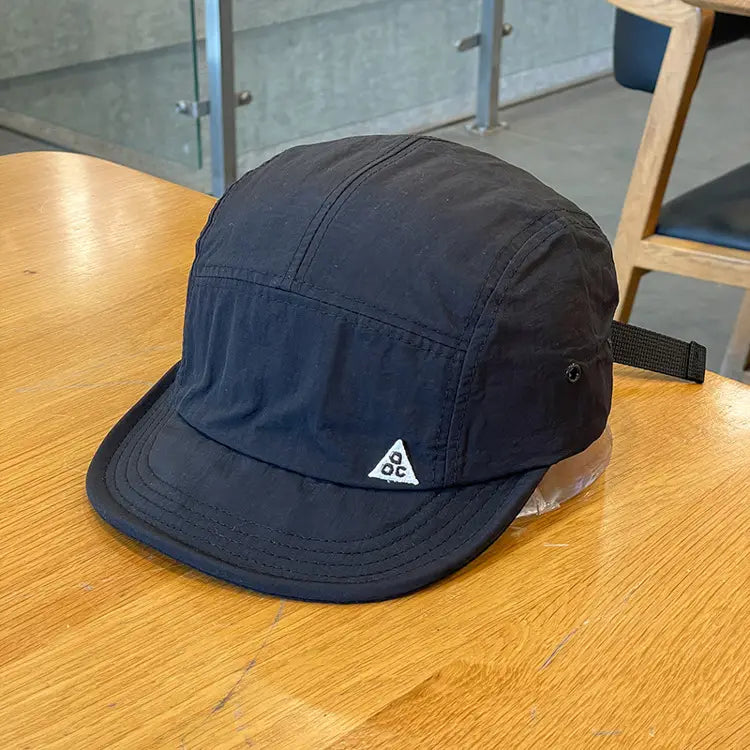 black quick drying five panel cap with a short brim and a white triangular logo on the front