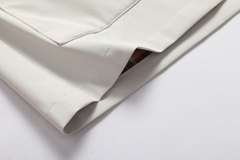 Stoff des Herren-Wasserabweisenden Trenchcoats mit Kapuze in Off-White mit sauberem Steppmuster und dezentem Schimmer, hergestellt aus einem leichten Baumwoll- und Synthetikgemisch.