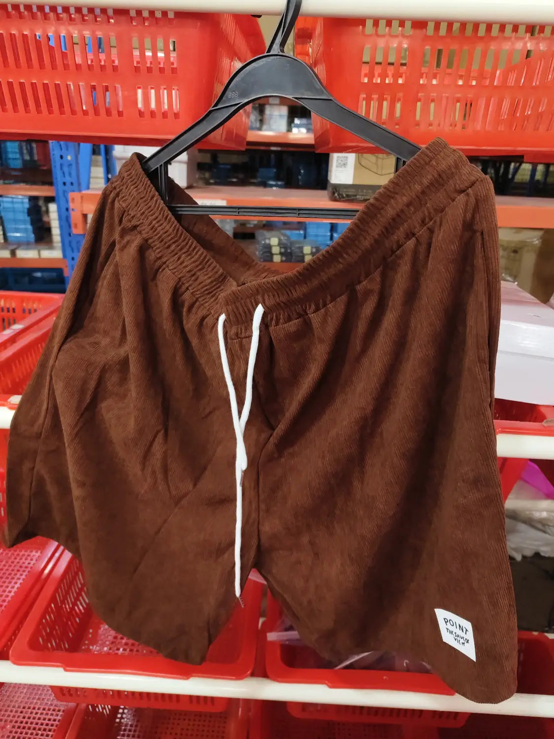 Shorts en velours côtelé marron à cordon de serrage pour hommes, avec des cordons de serrage blancs et une petite étiquette de marque « point » sur la partie inférieure droite de la jambe, conçus comme des pantalons de sport.