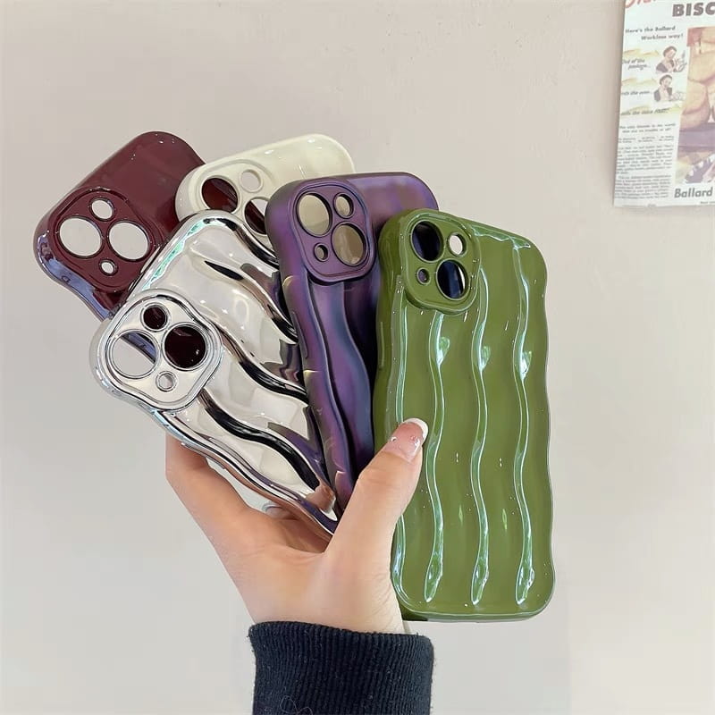 A hand holds a collection of glossy wavy liquid silicone iPhone cases in maroon white silver purple and olive green showing the back side of the cases.