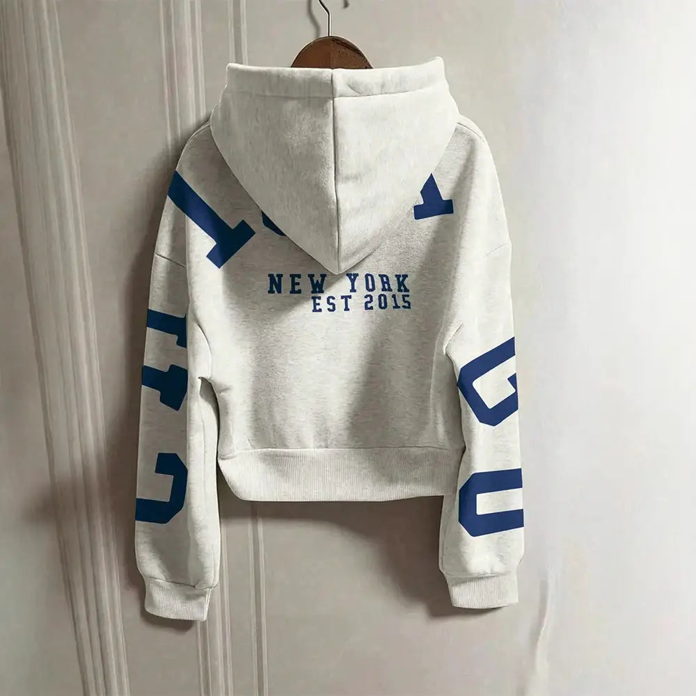 Sweat-shirt à capuche zippé imprimé graphique blanc court, avec une inscription bleue en lettres majuscules et un graphique « New York Est 2015 » au dos, présentant des poignets et un bas côtelés.