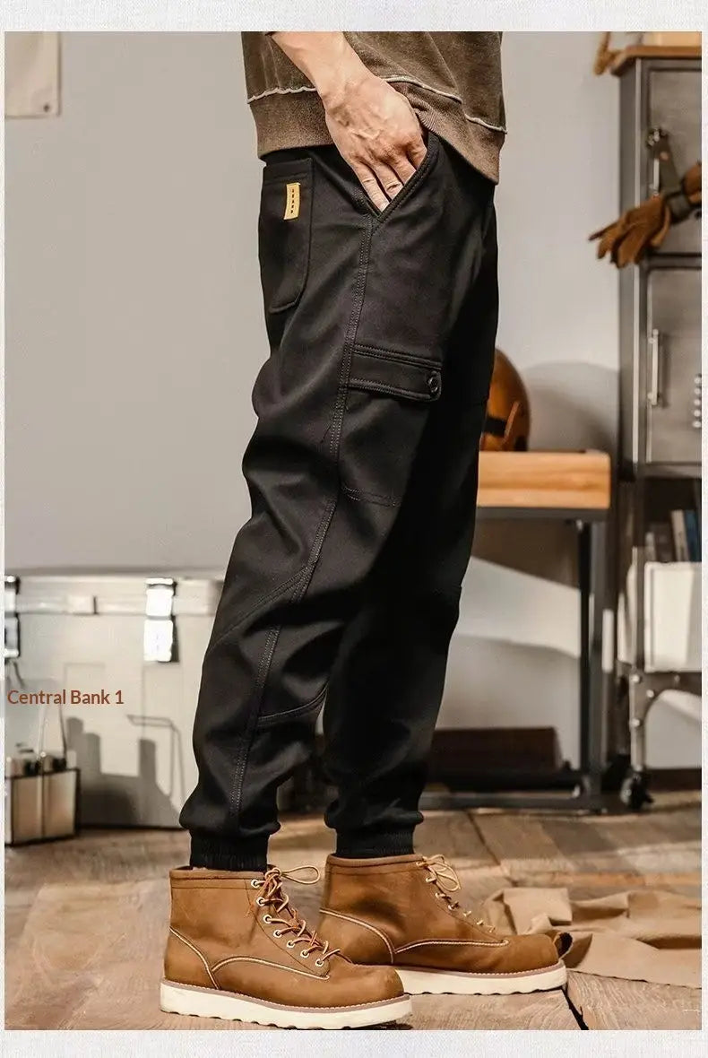Pantalons cargo pour hommes à coupe ample, style décontracté et vêtement de travail, en noir, avec plusieurs poches et une étiquette de marque jaune discrète sur la cuisse.