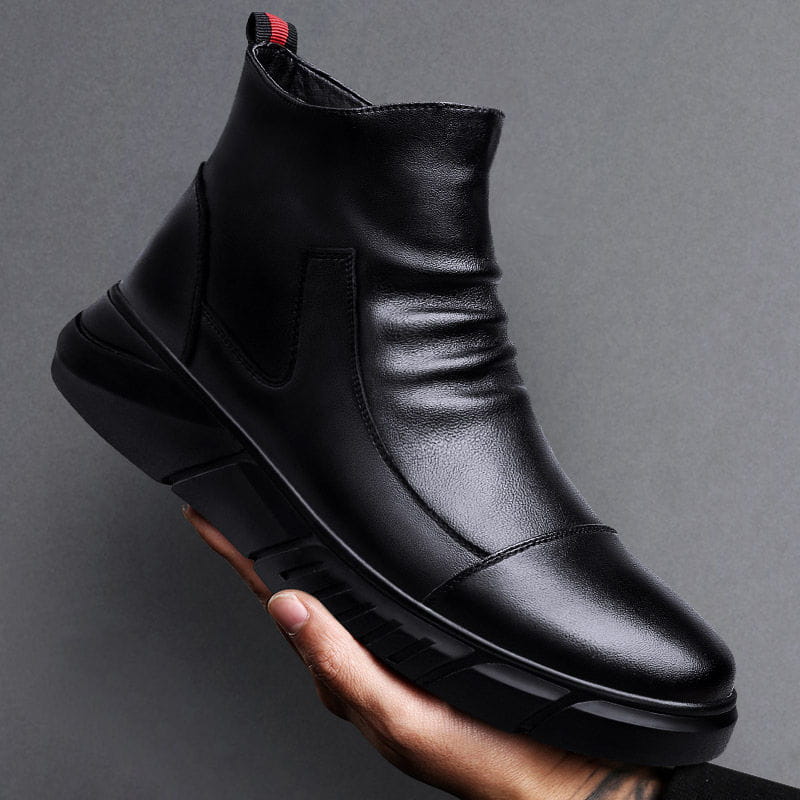 Schwarzer Leder-Chelsea-Boot mit hohem Schaft, kräftiger Gummisohle und rotem Akzent am Zugriegel, dargestellt von der Rückseite.