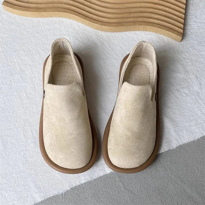 Beige Veloursleder-Slipper mit brauner Gummisohle mit Vintage-British-Charakter und niedrigem Absatz, dargestellt.