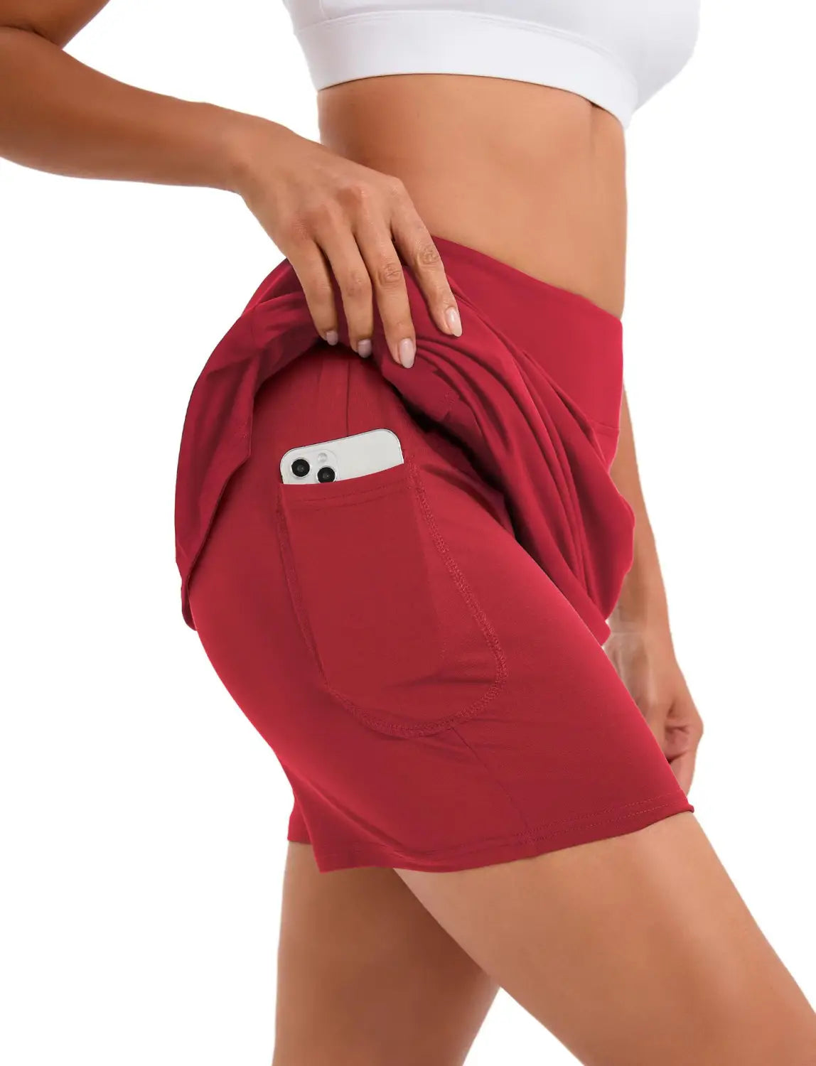 red high-waisted athletic tennis skirt featuring a side pocket holding a smartphone for convenient storage during sports activities.