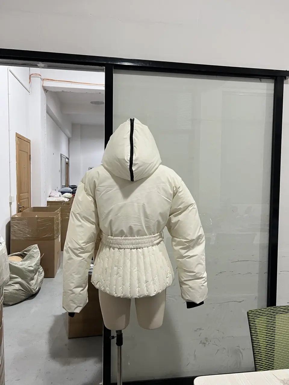the back side of a white belted hooded puffer coat featuring a black zipper and cinched waistband for women