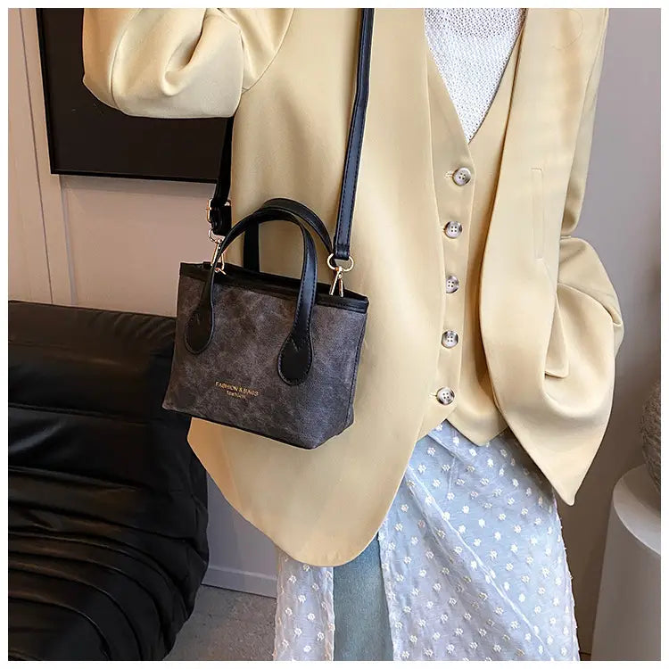 Black and gray patterned retro bucket bag mini handbag made of textured canvas with leather handles and shoulder strap.