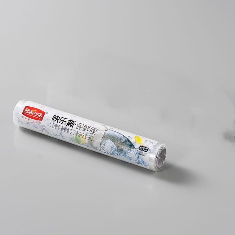 Eine Rolle transparente Kunststoff-Lebensmittelfolie mit der Marke kuai le si baoxian mo von jingpin shenghuo, mit einer Illustration von Fischen und Gemüse, dargestellt in einem magnetischen Kunststoff-Folienabschneider und -spender.
