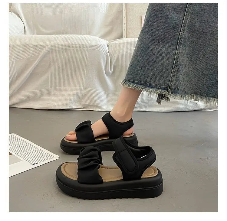 Sandales plateforme noires pour femmes présentant des brides en tissu froncées et une semelle épaisse texturée, vues de l’arrière.