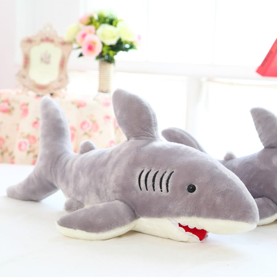 Gray plush shark toy with black eyes red stitched mouth teeth and gills and a white underbelly designed as a soft stuffed animal.