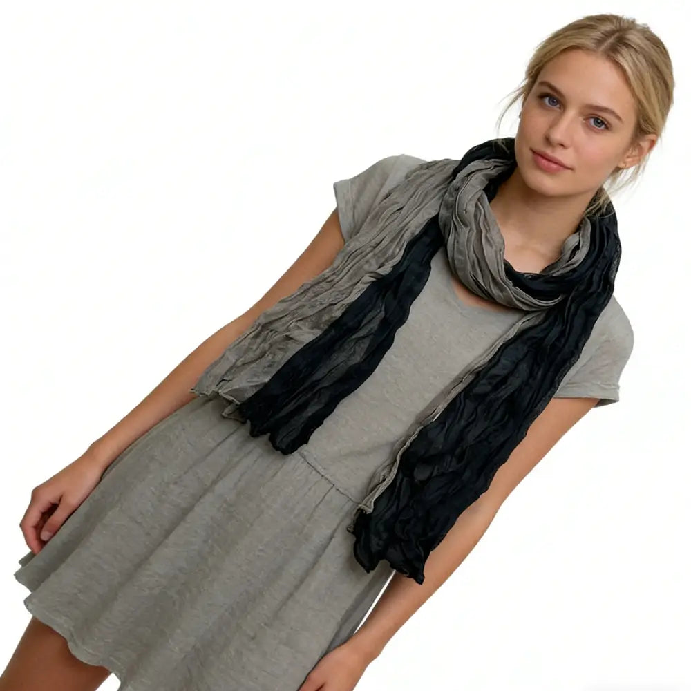 Una bufanda de color gris negro con textura y aspecto arrugado, con un degradado suave de gris oscuro a negro, drapeada con elegancia alrededor del cuello de la modelo.