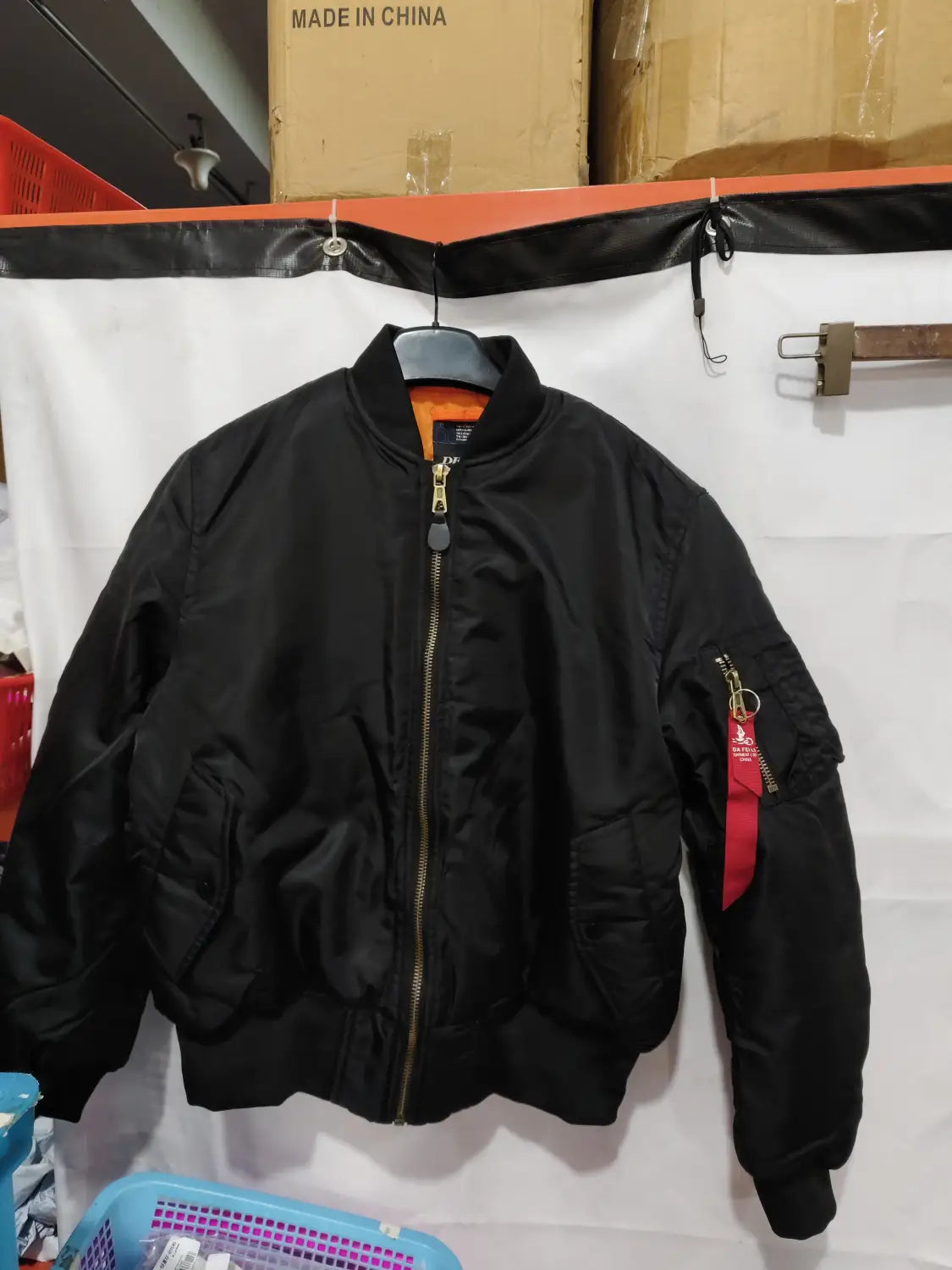 Men’s pilot cotton bomber jacket by Alpha Industries in black with orange lining and a red tag on the sleeve.