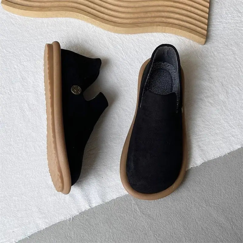 Schwarze Veloursleder-Slipper im Vintage-British-Stil mit niedrigem Absatz mit einer braun wirkenden Gummisohle und einem kleinen metallisch wirkenden Knopf an der Seite