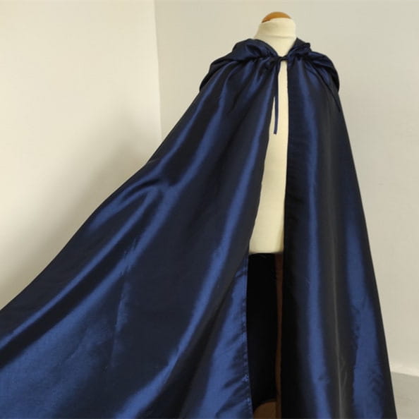 A deep navy satin cape with a tied hood and soft sheen displayed on a mannequin alongside a wooden cat tree scratching post and condo.
