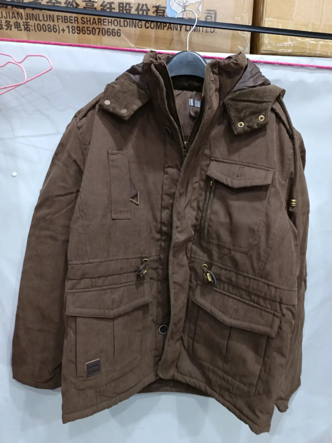 Chaqueta de invierno acolchada con forro polar para tallas grandes en pana marrón, con capucha, múltiples bolsillos con solapa y herrajes de tono dorado diseñados para el clima frío.