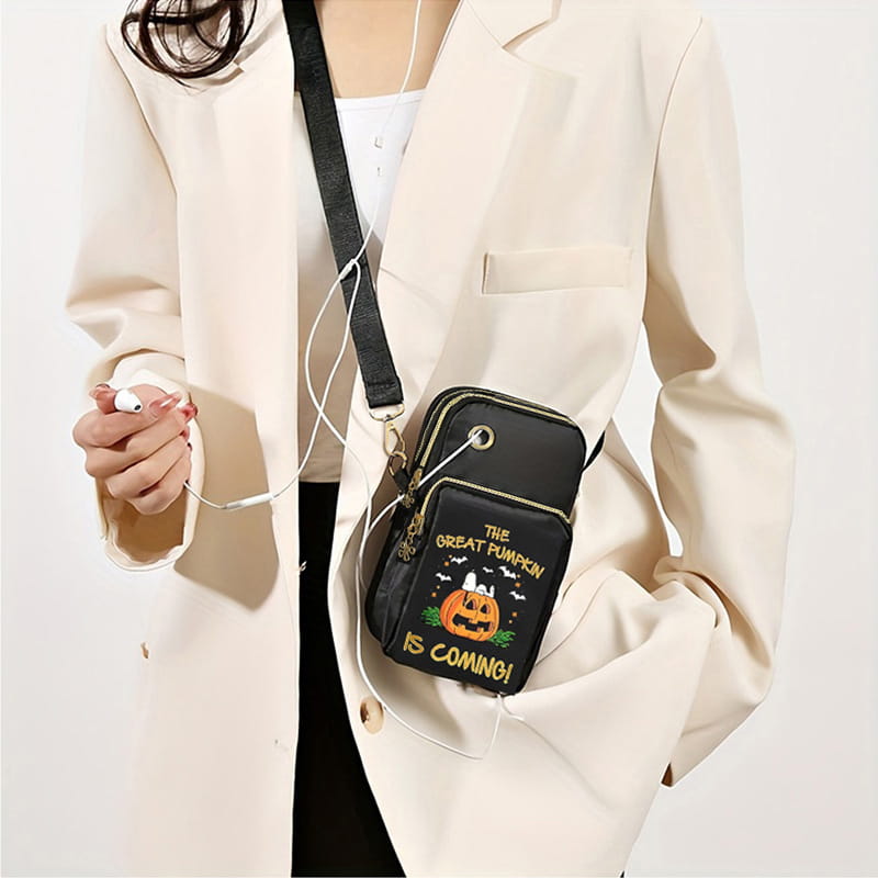 Black crossbody phone bag featuring embroidered Halloween design with a smiling pumpkin, bats, and the text the great pumpkin is coming in gold lettering in the Halloween pumpkin Snoopy embroidered crossbody phone bag.
