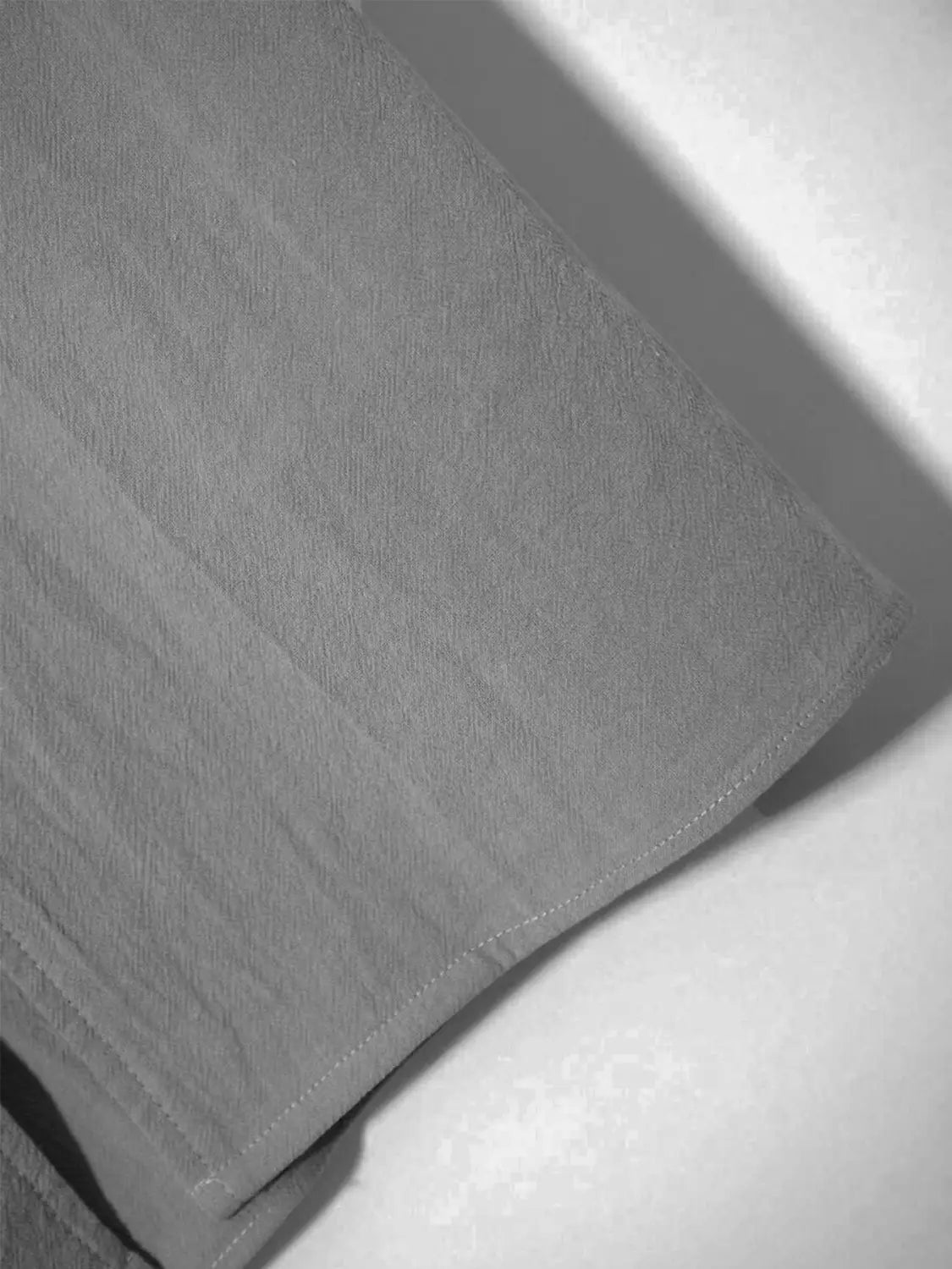 tissu en lin gris texturé, couture visible le long du bord, pour une chemise en lin boutonnée ample et décontractée pour homme.