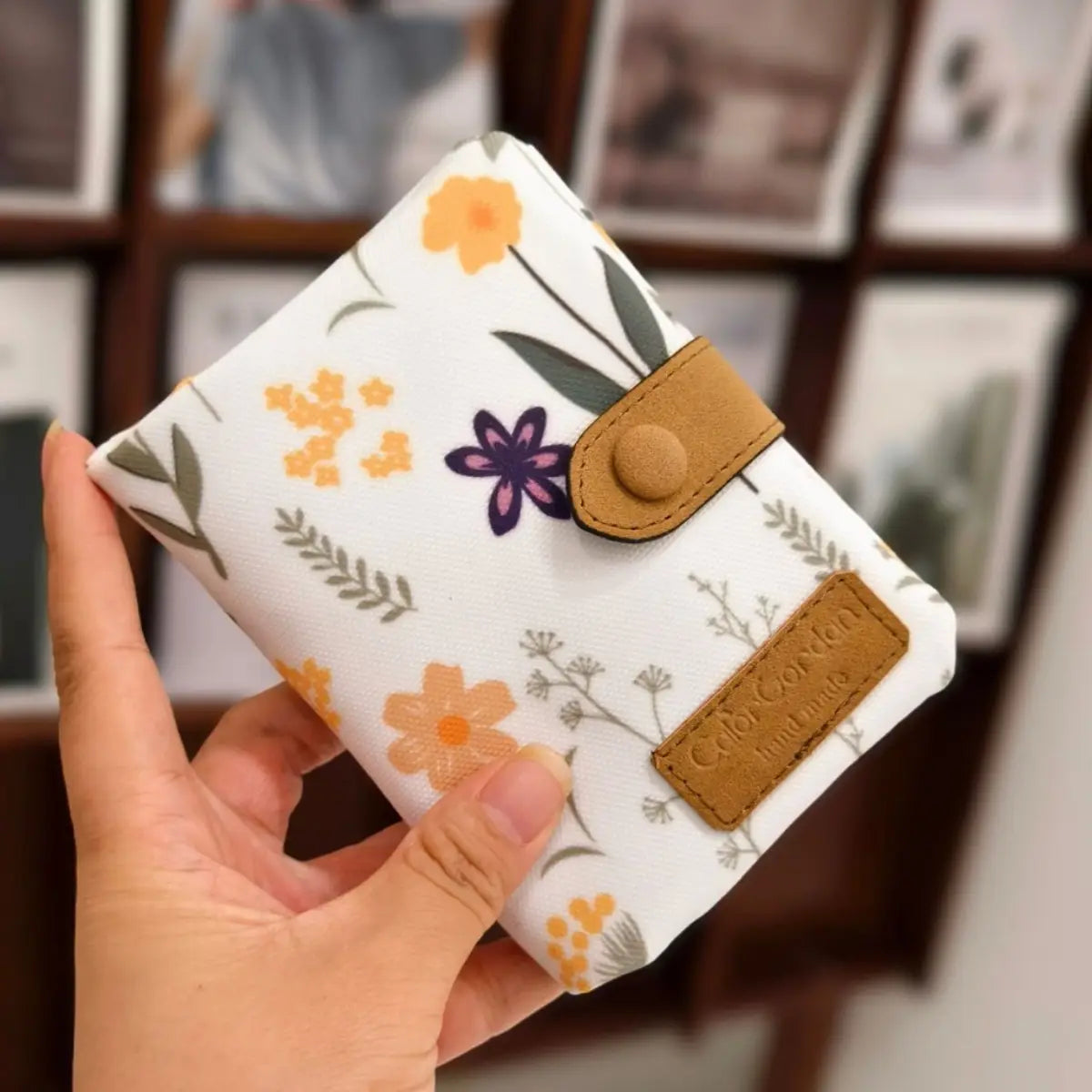 Whimsical patterned canvas tri fold multi card wallet in white floral pattern with tan leather accents and button closure.