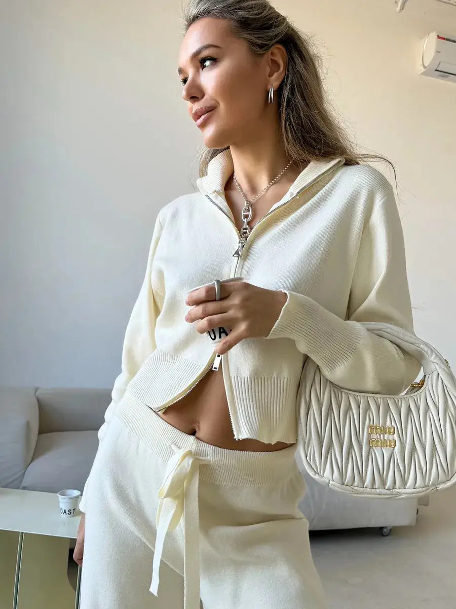 cream-colored quilted handbag with gold-tone logo plaque paired with women’s knit zip up cardigan and wide leg pant set