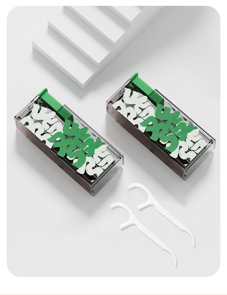 Dispensador automático de apertura emergente para caja portátil de hilo dental de plástico transparente, que contiene palillos dentales con forma de letras verdes y blancas, y dos picks blancos separados de hilo dental para un cuidado bucal conveniente.