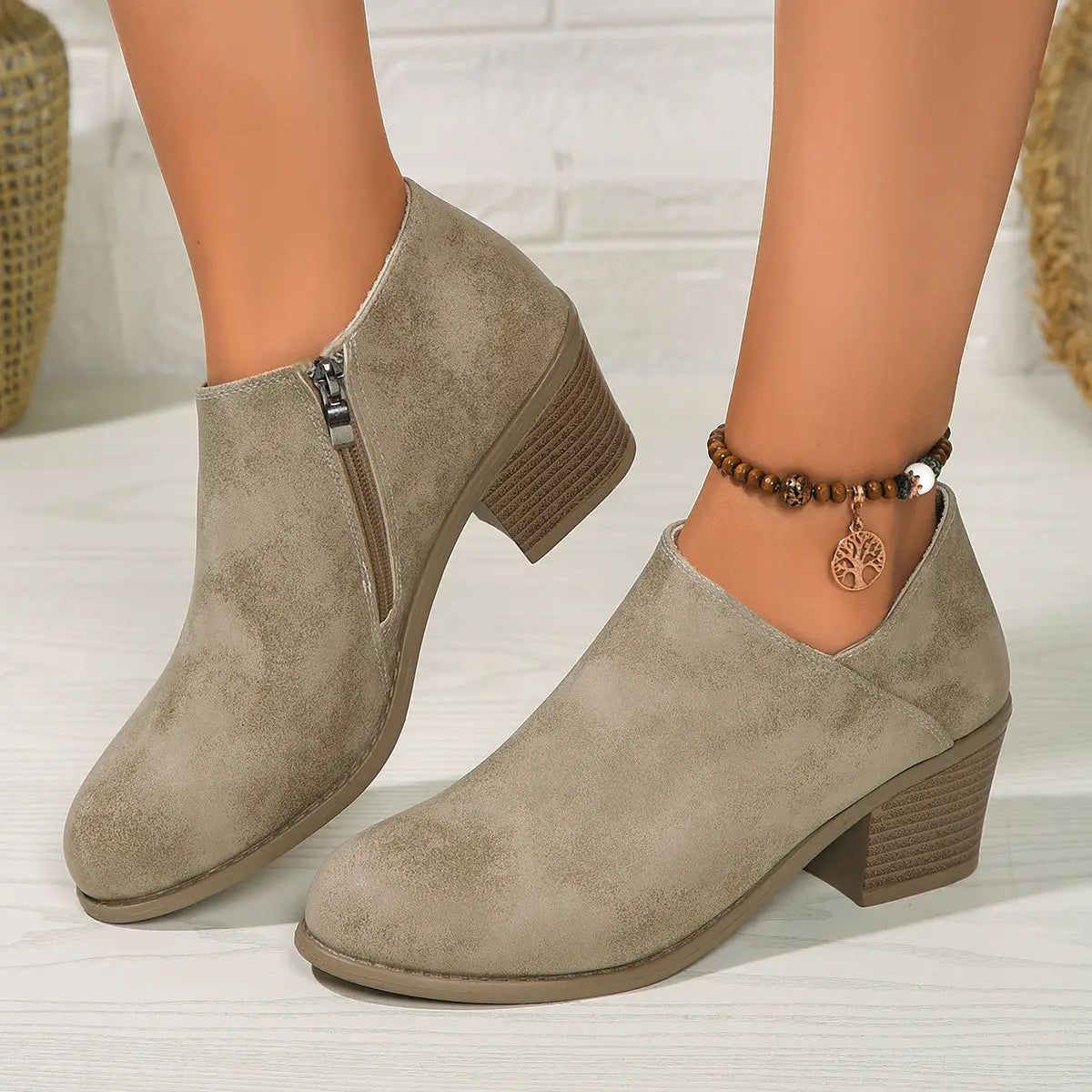 beige suede ankle boots with a chunky stacked heel and side zipper shown from the back side