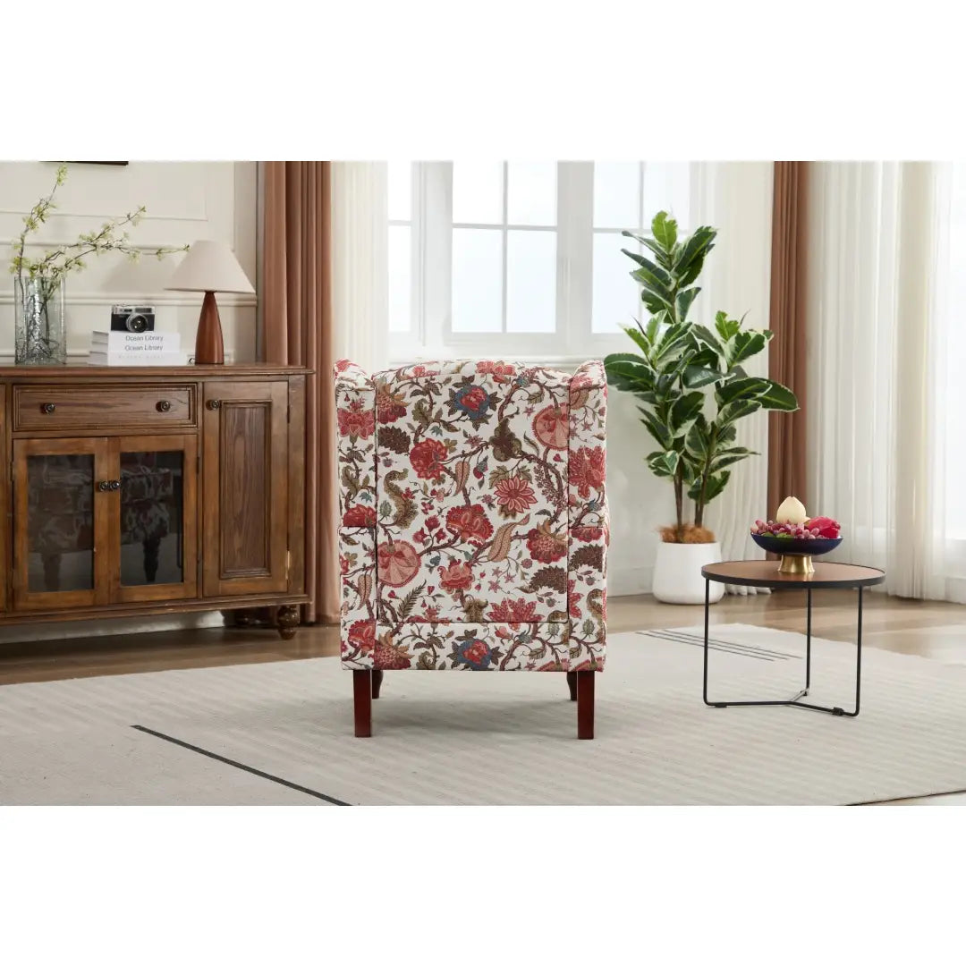 Una silla tipo ala con respaldo capitoné floral, tapizada en un tejido con flores rojas y marrones sobre un fondo color crema y con patas de madera retro.