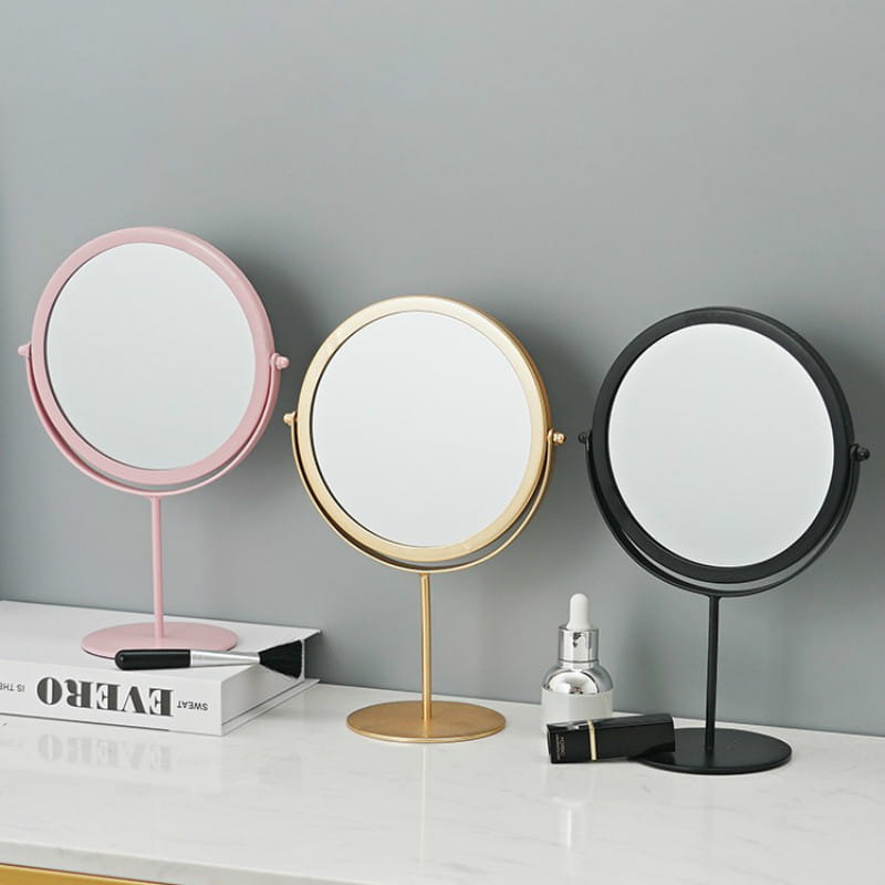 Three round vanity mirrors with slender stands and matching metallic frames in pink, gold, and black designed for makeup desk use.