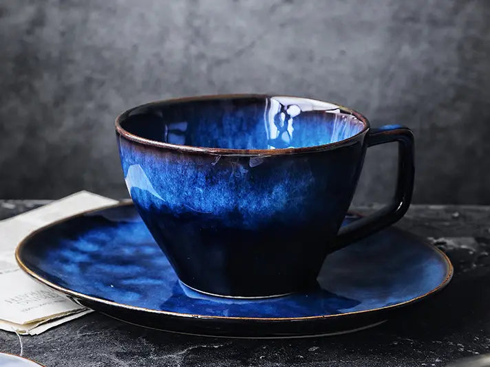 A deep blue ceramic coffee mug and matching saucer set featuring a glossy gradient glaze.
