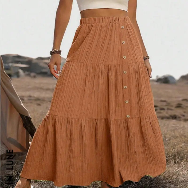 A flowing rust-colored tiered maxi skirt with a gathered waistband and button front closures made of lightweight material for casual wear.