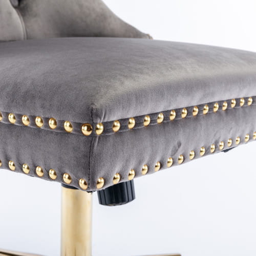 Chaise de bureau en velours capitonné gris avec garniture à clous décoratifs ton sur ton or et piètement pivotant sur colonne de couleur laiton.
