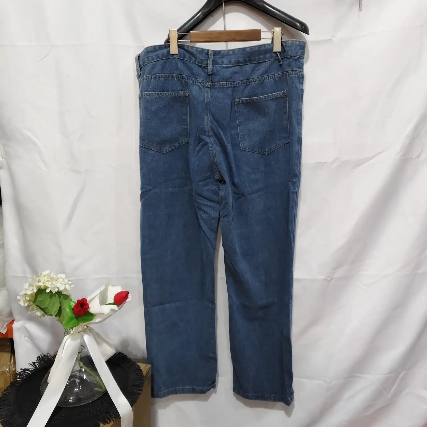 Jeans de mezclilla (denim) lavada de pierna recta para mujer en azul, con un diseño clásico de bolsillos traseros, mostrado desde la parte posterior, colgados en una percha de madera
