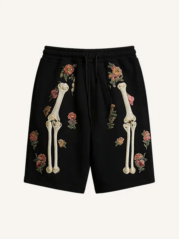 Black polyester sweat shorts featuring embroidered cream-colored skeleton legs and pink floral accents titled skeleton floral sweatshorts embroidered men.