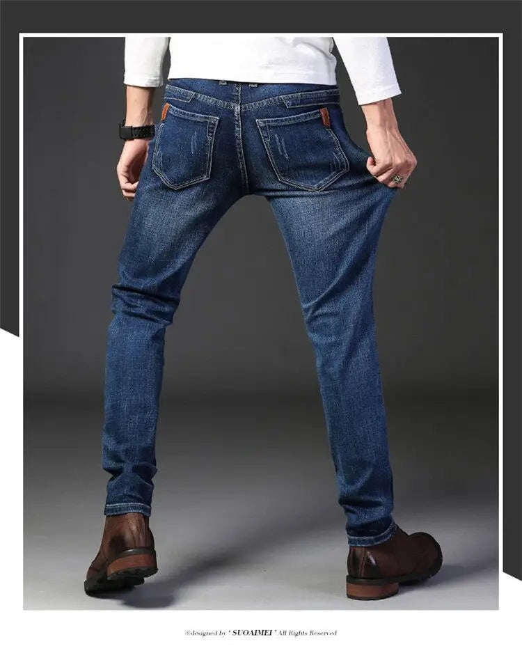 pantalones vaqueros de mezclilla elástica de corte slim fit para hombre, de lavado oscuro, rectos, que muestran el lado posterior, con parches de cuero marrón en los bolsillos traseros y un sutil desvanecido en la tela de mezclilla azul marino oscuro.