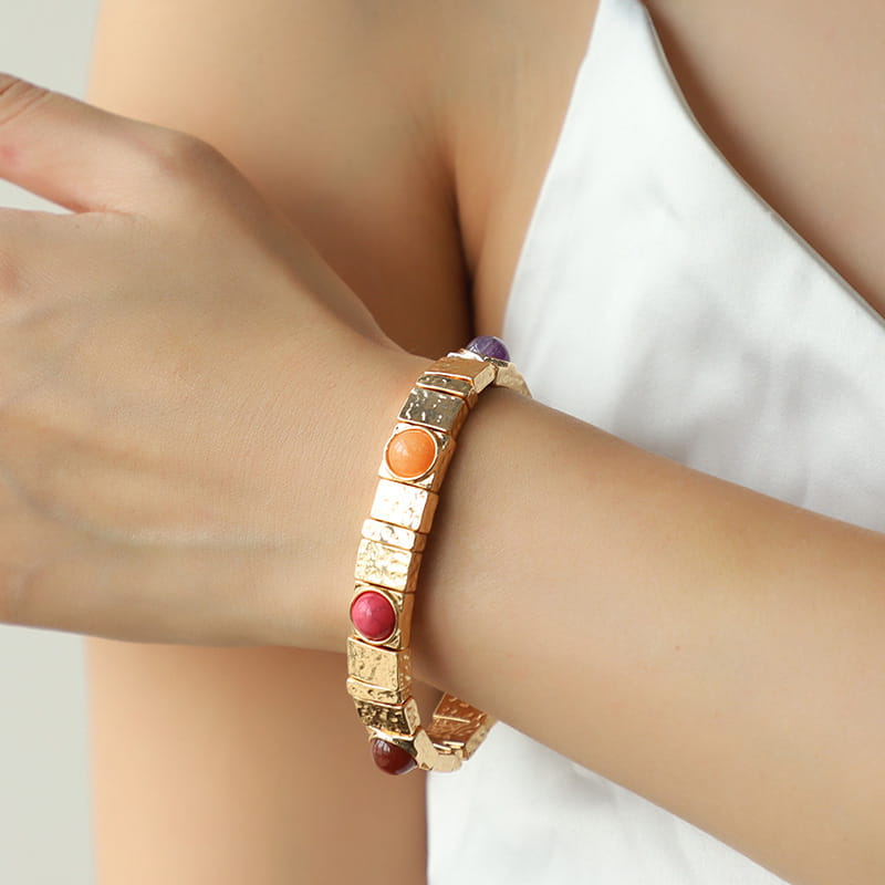 Vintage hammered gold bangle featuring rectangular textured segments and colorful round gemstones in orange red and purple.
