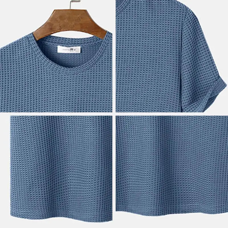 Herren-T-Shirt in Slim-Fit aus blauem Waffelstrick-Baumwollstoff als Henley mit kurzen Ärmeln und Rundhalsausschnitt, auf einem Holzkleiderbügel hängend.