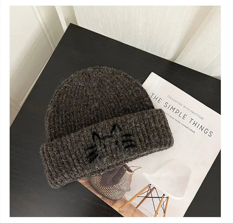 A cozy dark gray knitted beanie hat with a ribbed brim featuring a black embroidered cat face design.