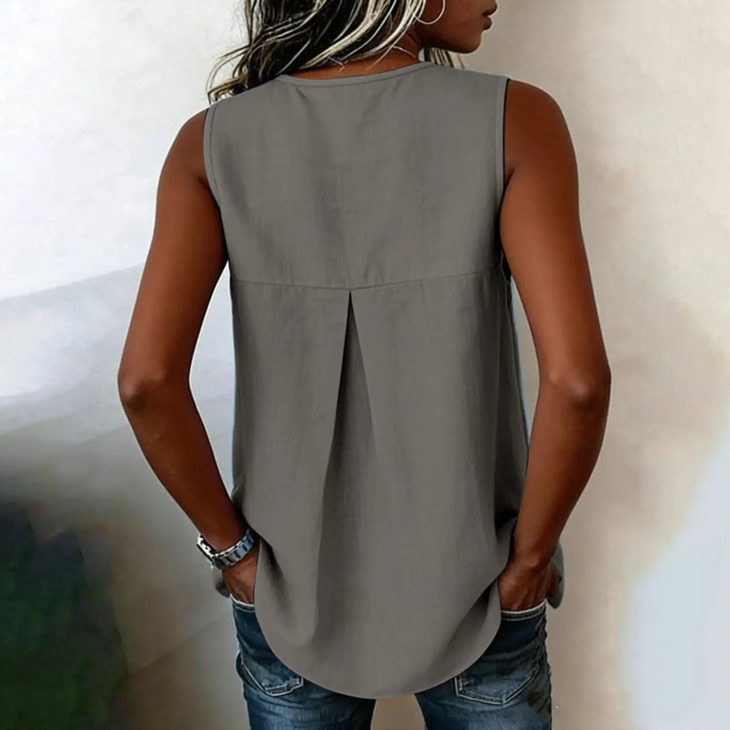 A sleeveless gray high-low cut blouse with tie side button down and a subtle pleat detail at the back shown from the back side.
