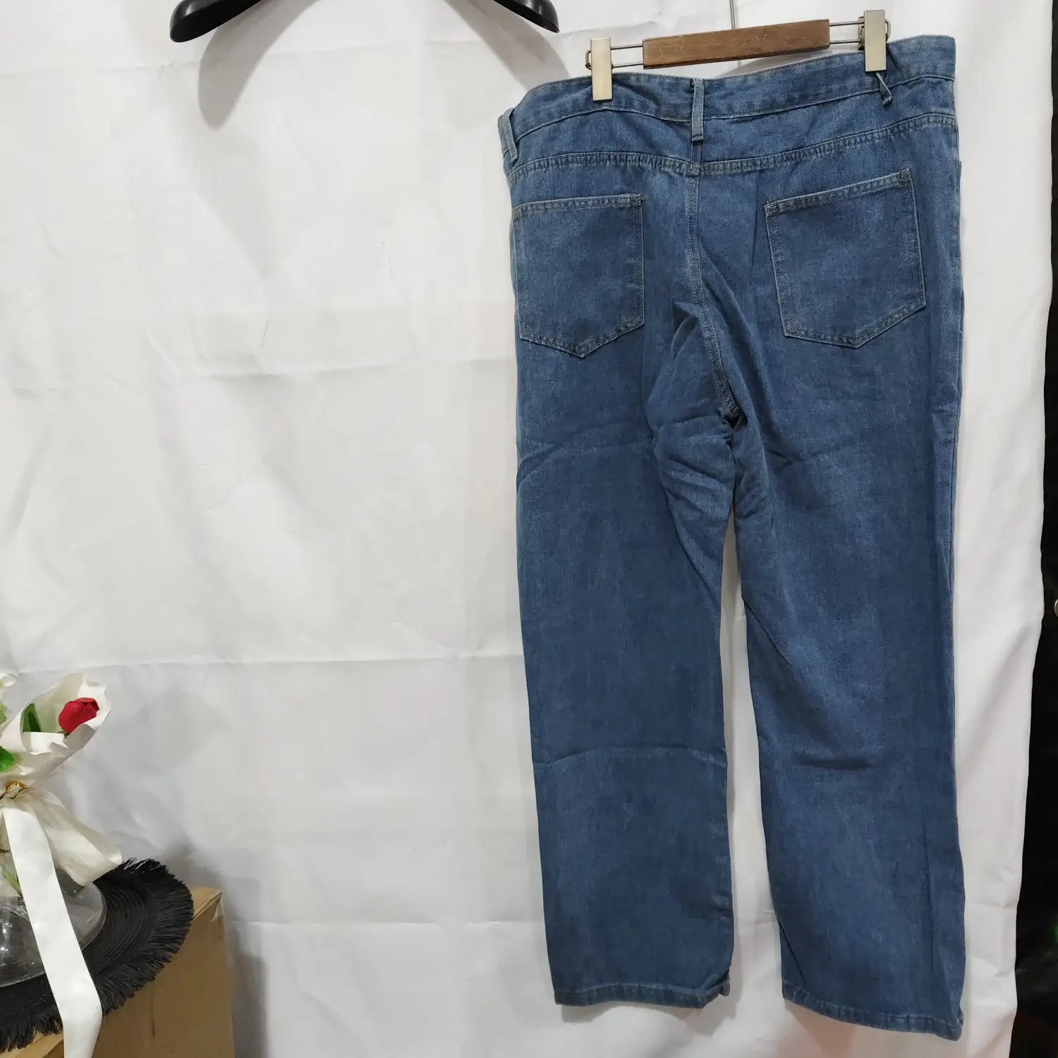 Jeans de mezclilla (denim) lavada de pierna recta para mujer en azul, con un diseño clásico de bolsillos traseros, mostrado desde la parte posterior, colgados en una percha de madera