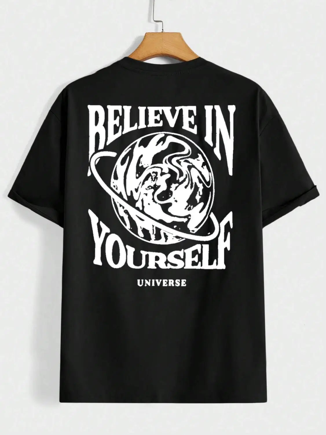 Schwarzes Baumwoll-Herren-T-Shirt mit kurzen Ärmeln und weißem Believe-in-Yourself-Graphic-Print mit einer Planetenillustration, die an einem Holzbügel hängt.