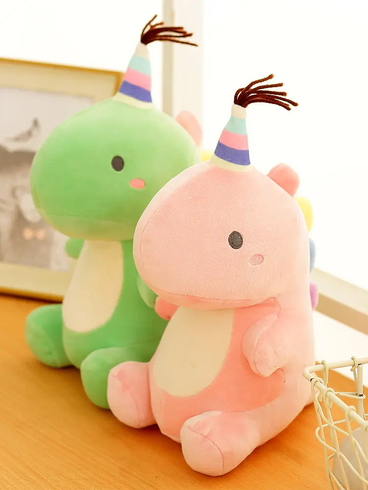 Ein pinkfarbener Dinosaurier-Plüschtier mit einer regenbogen-gestreiften Party-Kappe und weichem braunem, lockig aufgesetztem Haar – als Kuscheltier gefüllt.