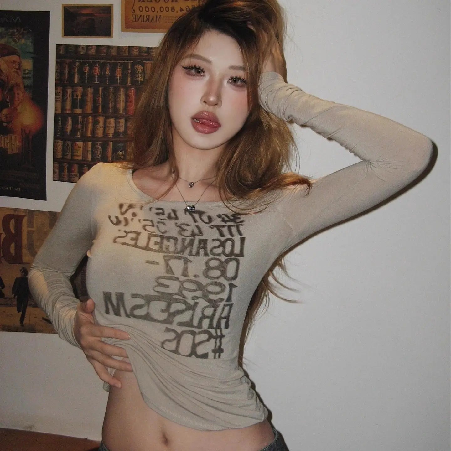 A beige sheer fitted long sleeve crop top with black graphic letter print across the front.