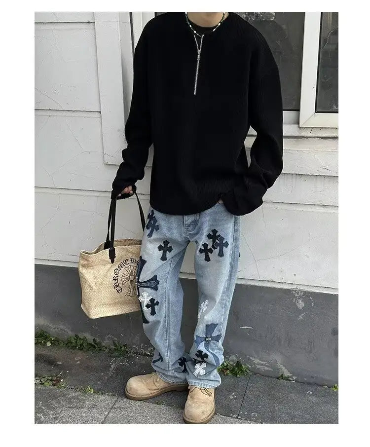 Jeans de mezclilla de lavado claro con patrones cruzados bordados en negro y blanco, combinados con una sudadera tipo jersey acanalada de media cremallera para hombre.