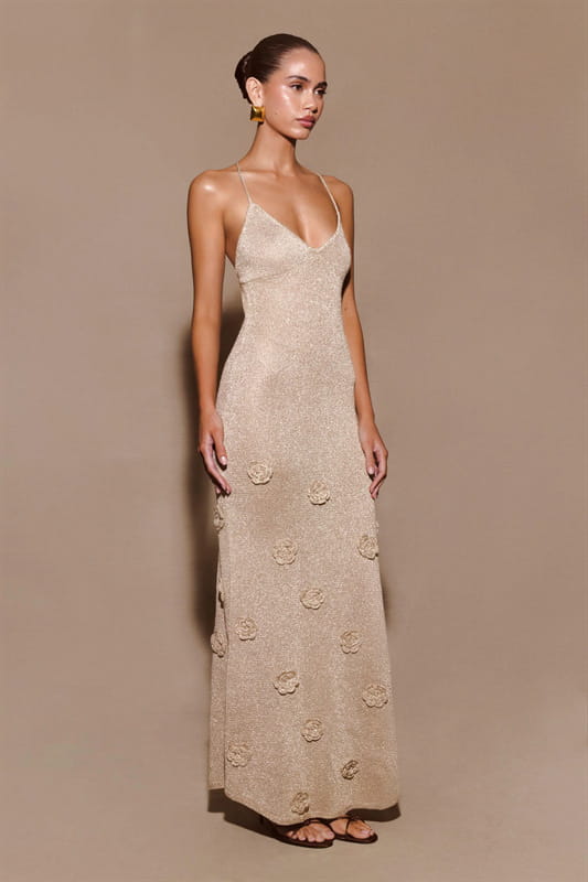A beige crochet floral lace mermaid maxi dress with glitter accents featuring delicate spaghetti straps v-neckline and subtle floral embroidery along the skirt.