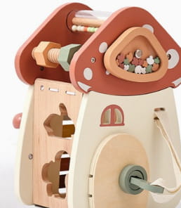 Maison en jouet en bois charmante, avec un toit rouge, des murs beige et des accents en bois naturel, présentée dans le jouet pour cube d’activités en bois à 5 en 1.