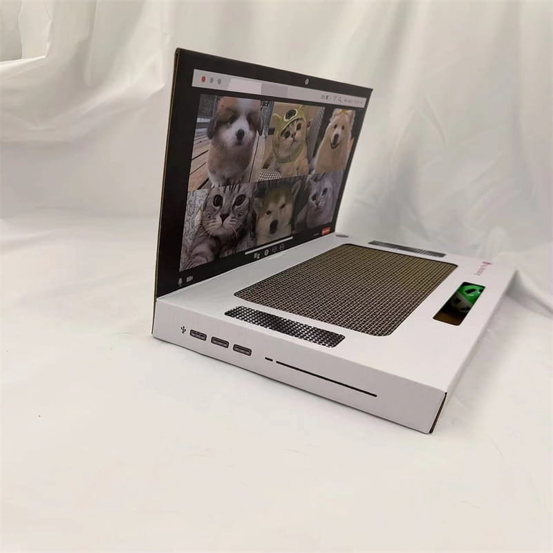Weißer, laptopförmiger Pappkarton-Katzenkratzer mit strukturierter Kratzoberfläche im Tastaturbereich und einem Bildschirm, der Fotos von Hunden und Katzen zeigt.