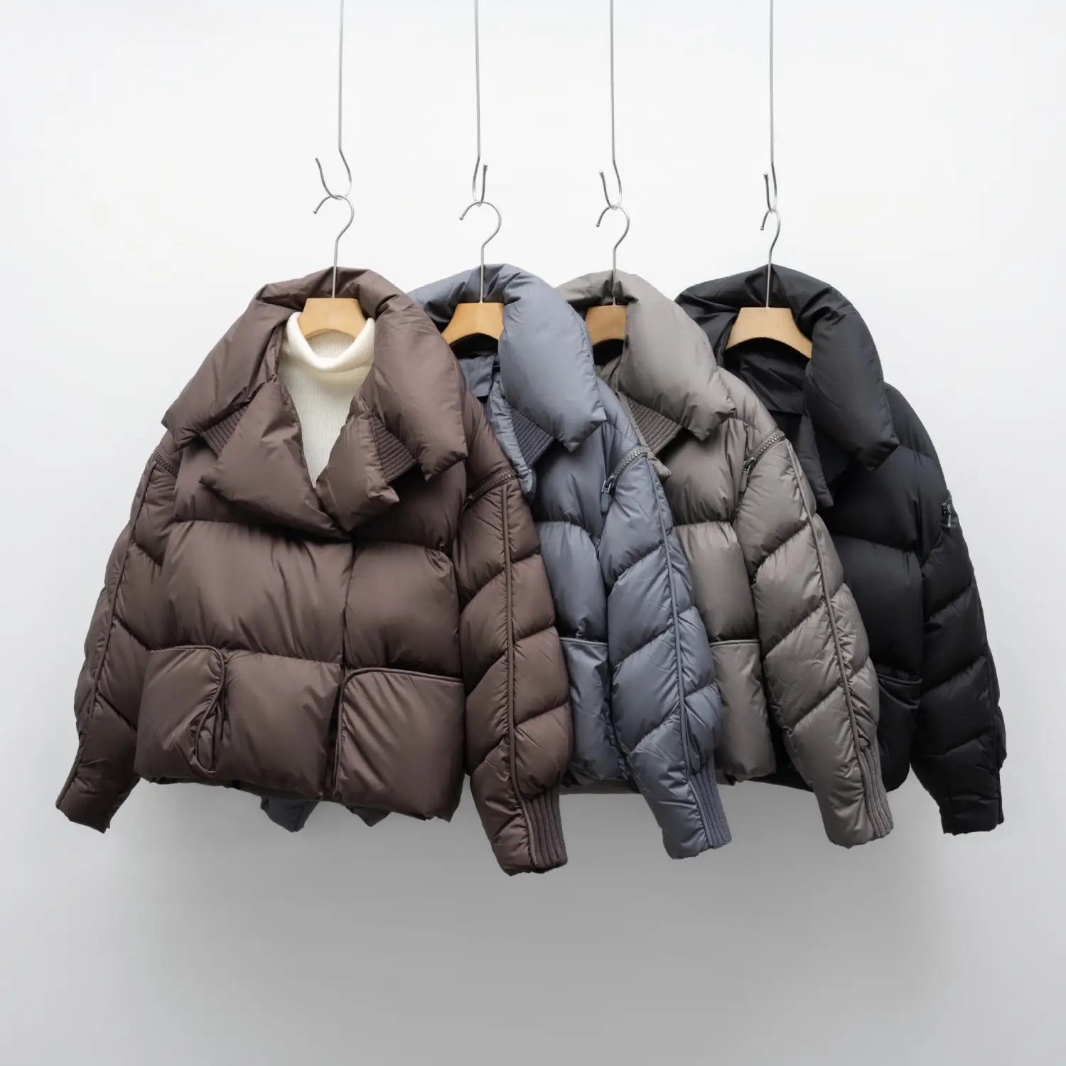 Four down jacket patchwork large lapel Korean style puffer jackets in brown gray and black hang on wooden hangers against a white background.