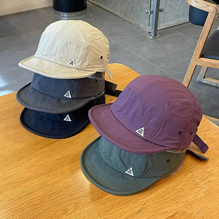 Quick drying short brim five panel hats in beige, dark gray, navy blue, and purple featuring a small white triangular logo on the front.