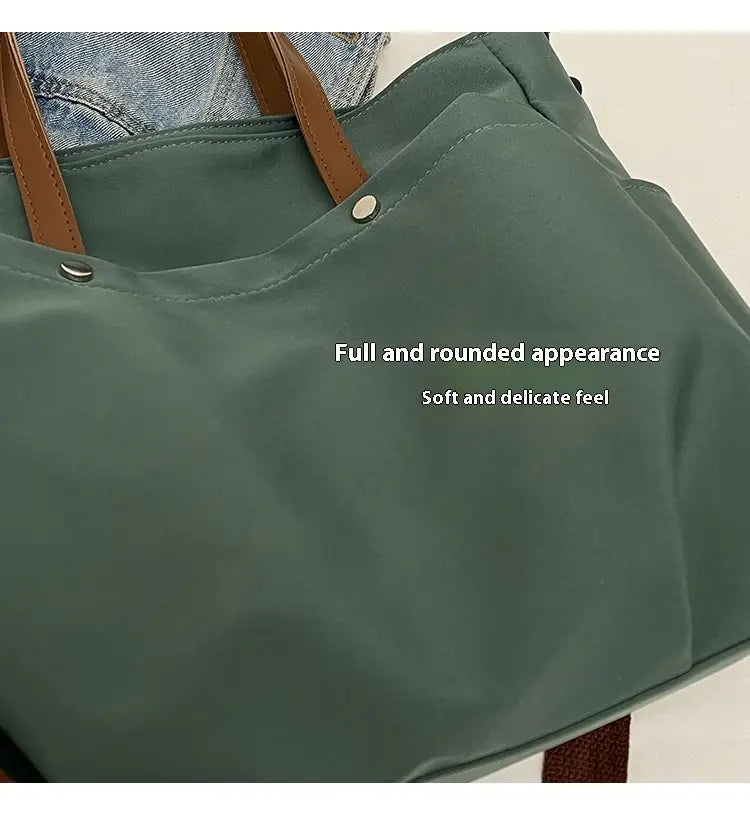Olive green large capacity canvas tote bag made of nylon with brown leather handles and silver toned metal hardware.